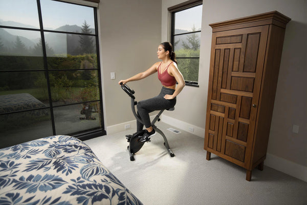 Woman exercising on a stationary bike in a bedroom with a wooden wardrobe.