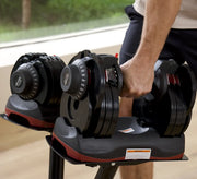 A close-up of a person lifting an adjustable dumbbell from a black and red weight rack in a gym setting.