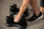 User adjusting Spark Adjustable Dumbbells - Women Beginners | Easy Use, 27.5 Lbs on textured floor, highlighting easy-to-use weight change dial.