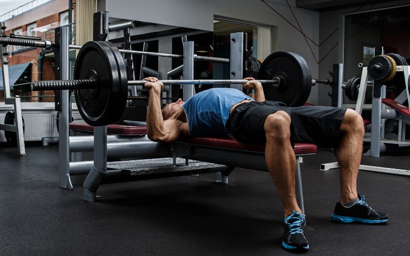 A man performing a bench press exercise with a barbell in a modern gym, focusing on chest workout intensity and proper lifting technique.