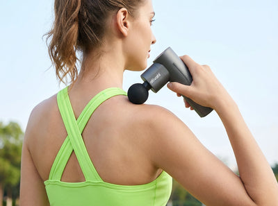 Woman using a massage gun on her shoulder outdoors