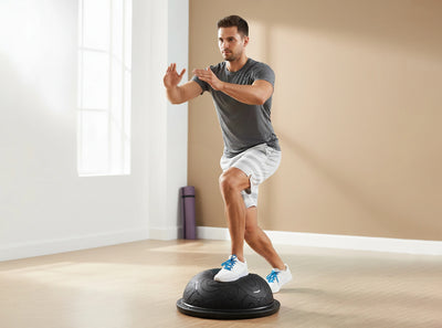 Man exercising on a balance trainer in a home setting