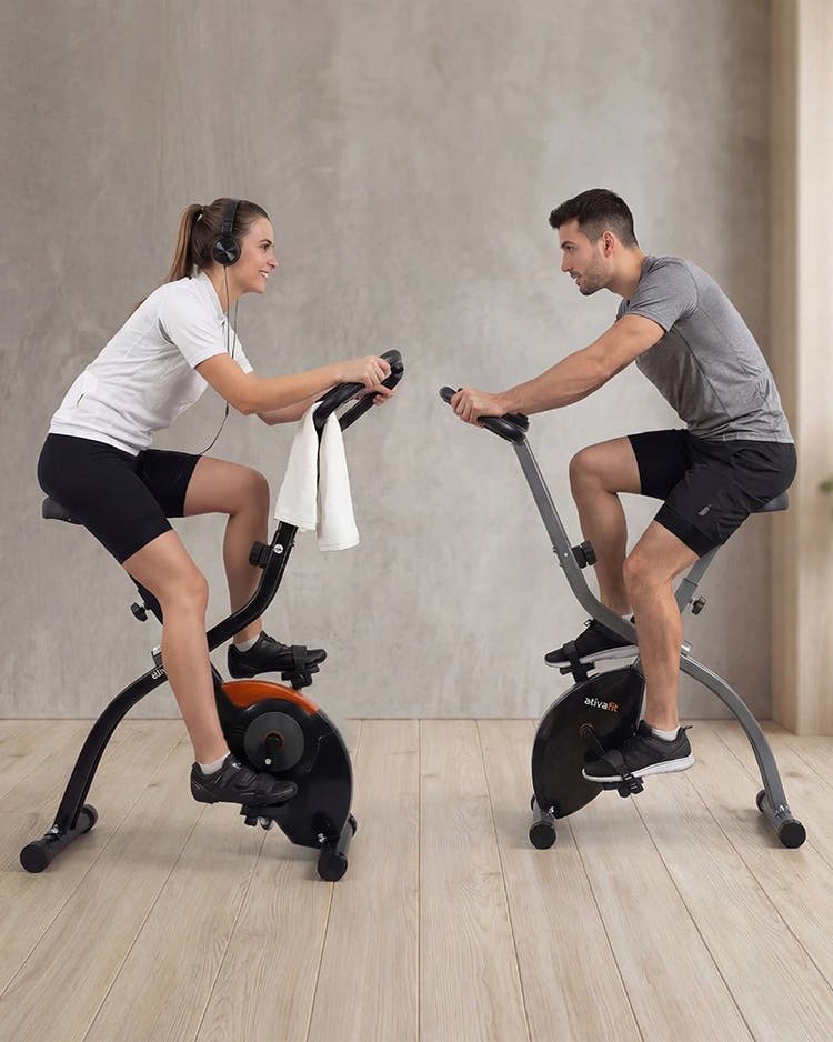 Two people exercising on stationary foldable bikes in a home setting.
