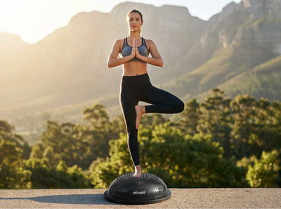 Woman practicing yoga on a half balance ball with mountains and trees in the background