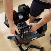 A close-up of a person adjusting a black adjustable dumbbell on a weight bench in a gym setting.